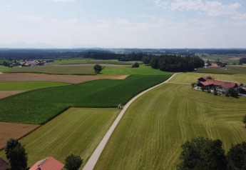 Landscape view showing green fields, a winding road, and an Almhütte chalet surrounded by farmland.