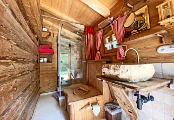 Rustic wooden bathroom at Almhütte chalet in Germany featuring a stone sink, shower, and red curtains.
