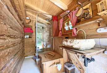 Rustic wooden bathroom at Almhütte chalet in Germany featuring a stone sink, shower, and red curtains.