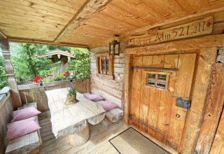 Landelijke houten veranda van een Duitse Almhütte met banken, tafel, kussens en bloemen.