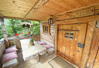 Rustic wooden porch of a German chalet Almhütte with benches, table, pillows and alpine flowers.