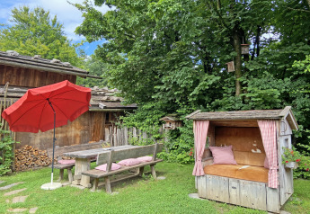 Garden area at the chalet 'Almhütte' in Germany, featuring wooden benches, red umbrella and a cozy nook.