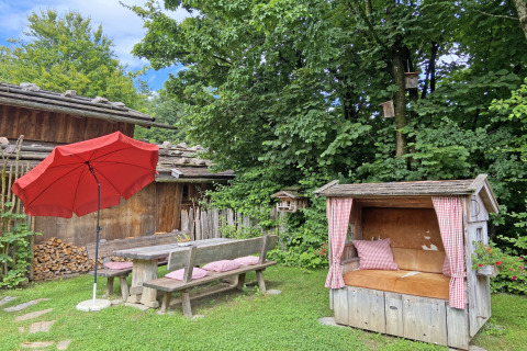 Tuin bij chalet 'Almhütte' in Duitsland, met houten banken, rode parasol en een gezellige zithoek.