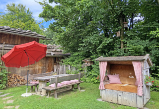 Tuin bij chalet 'Almhütte' in Duitsland, met houten banken, rode parasol en een gezellige zithoek.