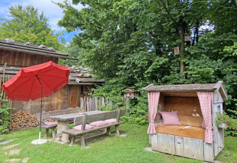 Garden area at the chalet 'Almhütte' in Germany, featuring wooden benches, red umbrella and a cozy nook.