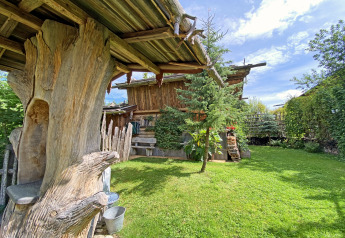 Rustic Almhütte chalet in Germany with wooden beams, lush green lawn, trees and a bright, sunny sky.