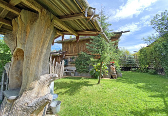 Rustic Almhütte chalet in Germany with wooden beams, lush green lawn, trees and a bright, sunny sky.
