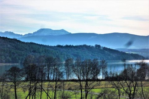 Uitzicht vanop chalet Almhütte in Duitsland met een meer, bergen, grasvelden en kale bomen vooraan.