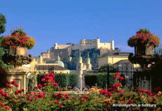 Wunderschöner Blick auf den Mirabellgarten in Salzburg mit Blumen, Springbrunnen und Festung im Hintergrund.