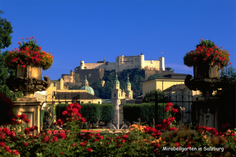 Prachtig zicht op de Mirabellgarten in Salzburg met bloemen, fonteinen en een historisch fort op de achtergrond.