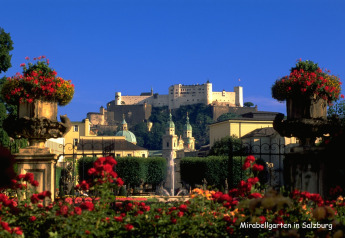 Beautiful view of Mirabellgarten in Salzburg with vibrant flowers, fountains, historic buildings, and a fortress.