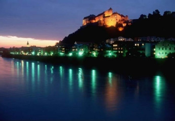 Evening view of an illuminated castle on a hill by the river, taken from Almhütte chalet in Germany.