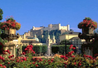 Vista di un giardino fiorito con una grande fortezza storica in cima alla collina sotto un cielo blu.