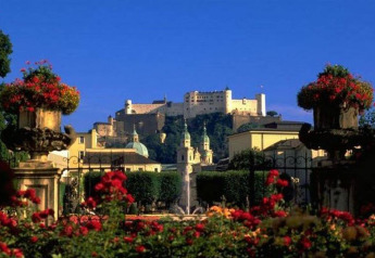 View of a lush garden with vibrant red flowers and a large historic fortress on a hill in the distance.