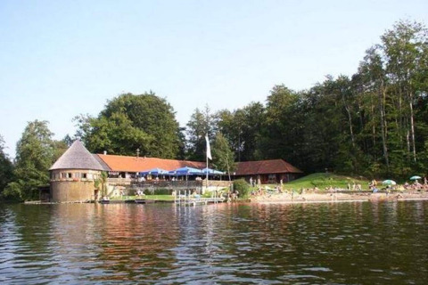 Gezicht op het Almhütte-chalet aan het meer in Duitsland met bezoekers en een bos op de achtergrond.
