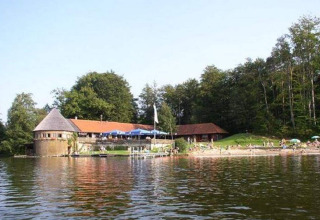 Gezicht op het Almhütte-chalet aan het meer in Duitsland met bezoekers en een bos op de achtergrond.