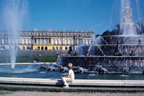 Springbrunnen vor Schloss Herrenchiemsee, Deutschland, mit Besuchern und prachtvoller historischer Fassade.