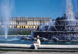 Springbrunnen vor Schloss Herrenchiemsee, Deutschland, mit Besuchern und prachtvoller historischer Fassade.