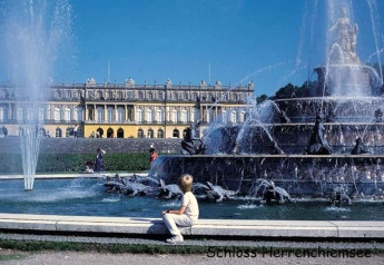 Fountain in front of Schloss Herrenchiemsee, Germany, with visitors enjoying the sun and grand palace façade.