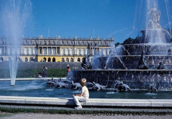 Fountain in front of Schloss Herrenchiemsee, Germany, with visitors enjoying the sun and grand palace façade.