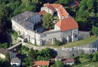 Luftaufnahme der Burg Tittmoning in Deutschland, umgeben von viel Grün und kleineren Gebäuden.