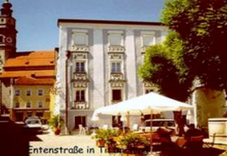 Foto von Entenstraße in Tittmoning, Deutschland, mit historischen Gebäuden, Sonnenschirm und gemütlichem Platz.