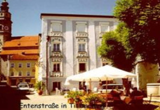Foto van Entenstraße in Tittmoning, Duitsland, met historische gebouwen en een zonnig gelegen buitencafé.