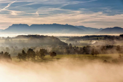Nebelverhangenes Panorama von der Almhütte in Deutschland mit Hügeln, Wäldern und Silhouetten der Berge.