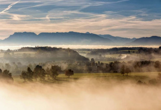 Nebelverhangenes Panorama von der Almhütte in Deutschland mit Hügeln, Wäldern und Silhouetten der Berge.