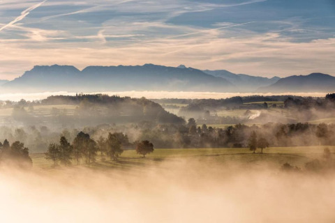 Mistig landschap vanaf chalet Almhütte in Duitsland met bergen, velden en bomen bij dageraad.
