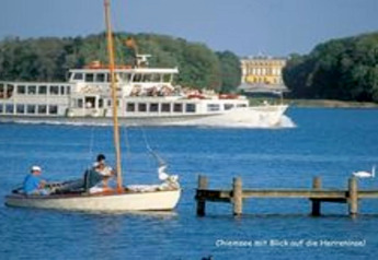 View of Chiemsee with boats and a ferry near the Almhütte chalet in Germany, palace visible in background.