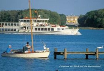 View of Chiemsee with boats and a ferry near the Almhütte chalet in Germany, palace visible in background.