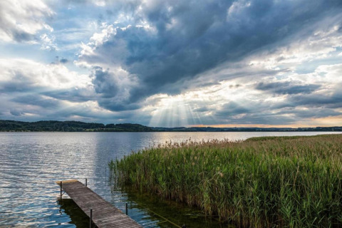 Zicht op een meer met houten aanlegsteiger, hoog riet en dramatische lucht nabij Almhütte, Duitsland.