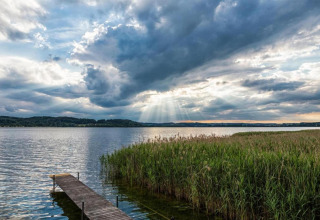 Zicht op een meer met houten aanlegsteiger, hoog riet en dramatische lucht nabij Almhütte, Duitsland.