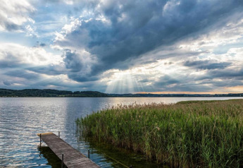 View of a lake with wooden pier, tall reeds, and dramatic sunset sky near Almhütte chalet, Germany.
