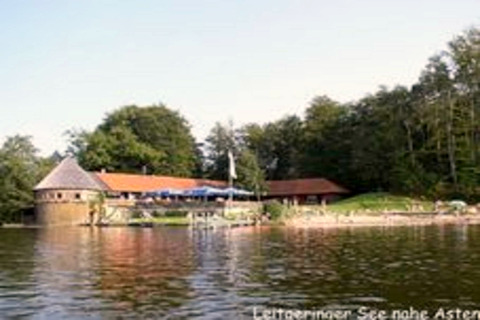 Chalet 'Almhütte' am See bei Ascheberg in Deutschland, umgeben von Bäumen, vom Wasser aus gesehen.
