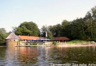 Chalet 'Almhütte' am See bei Ascheberg in Deutschland, umgeben von Bäumen, vom Wasser aus gesehen.