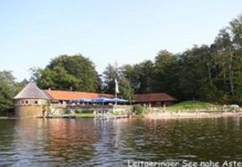 Chalet 'Almhütte' by the lake near Ascheberg, Germany, surrounded by forest and viewed from the water.