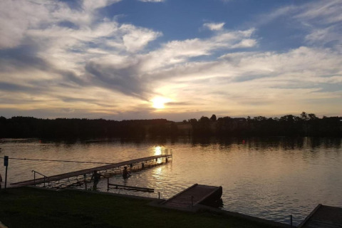 Avondzon bij chalet ‘Almhütte’ in Duitsland, met een steiger aan het water en wolken in de lucht.