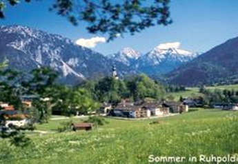 Summer view from Almhütte chalet in Ruhpolding, Germany with green fields, village houses and snowy mountains.