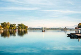 Blick auf den See bei der Almhütte in Deutschland mit Segelboot, Steg und Bergen im Hintergrund.