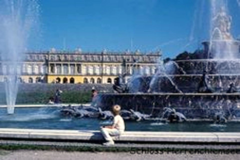 Springbrunnen und Schloss Herrenchiemsee in Deutschland, Besucher sitzen am Wasserrand an einem sonnigen Tag.