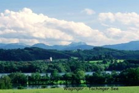 Blick von der Almhütte in Deutschland auf den Waginger-Tachinger See mit grünen Hügeln und Alpen im Hintergrund.