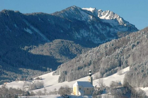 Winterlandschaft vom Chalet Almhütte in Deutschland mit verschneiten Bergen und einer Kirche im Tal.