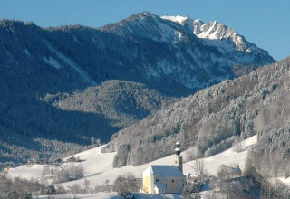 Winterlandschaft vom Chalet Almhütte in Deutschland mit verschneiten Bergen und einer Kirche im Tal.