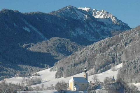 Winterlandschap vanaf chalet Almhütte in Duitsland met besneeuwde bergen en een kerk in het dal.