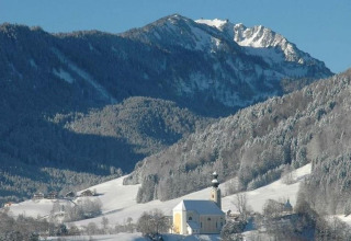 Winterlandschap vanaf chalet Almhütte in Duitsland met besneeuwde bergen en een kerk in het dal.