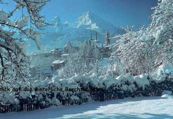 Winter scene from Chalet Almhütte in Berchtesgaden, Germany, showing snow-covered trees, village, and mountains.