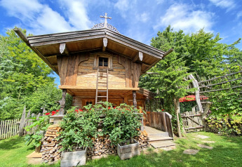Affascinante chalet di legno Almhütte con fiori, legna e verde sotto un limpido cielo azzurro.