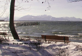 Vista sul Chiemsee da Chieming con riva innevata, panchine e montagne sullo sfondo in inverno.